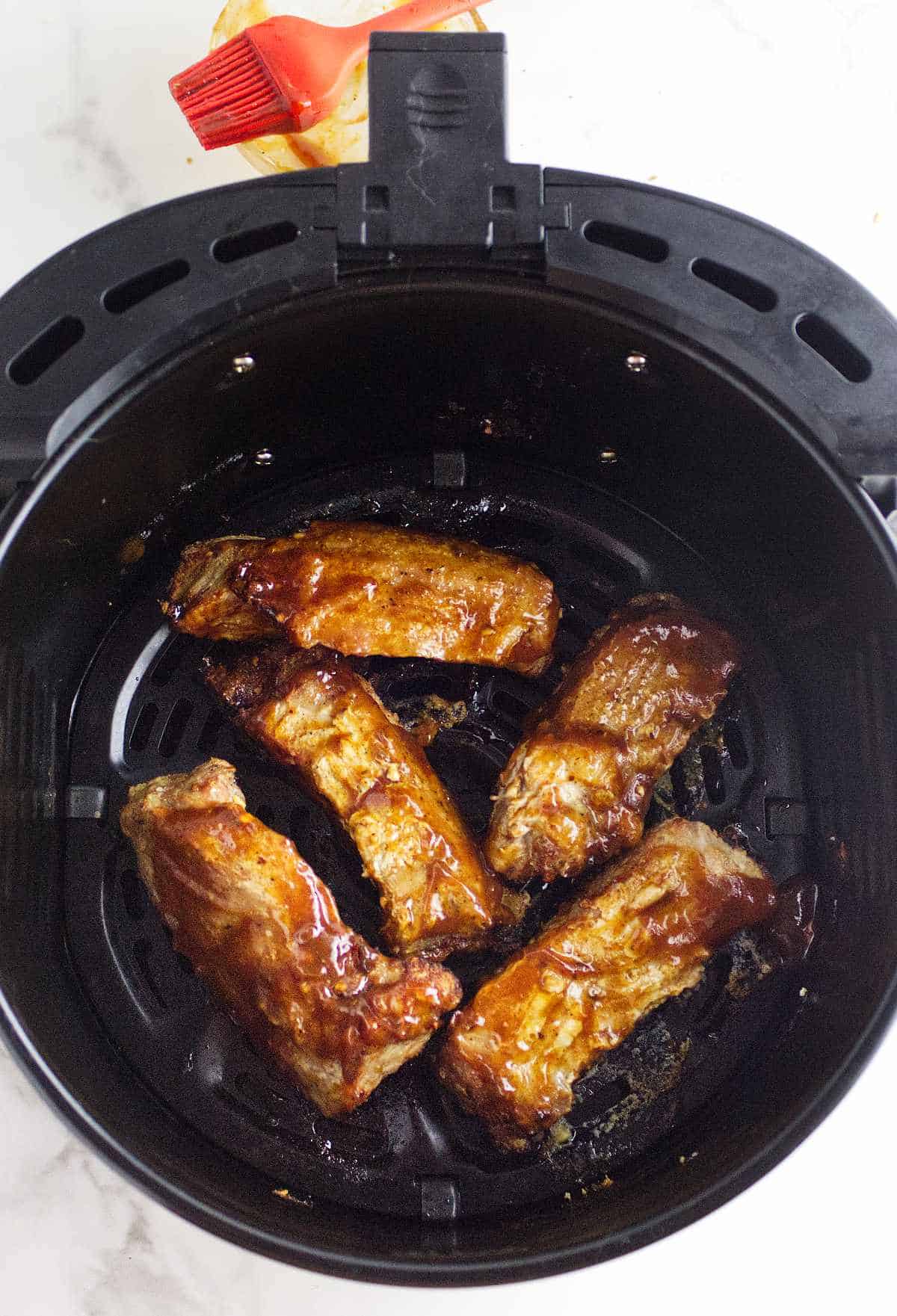 fresh barbecue sauce basted on cooked ribs in an air fryer basket.