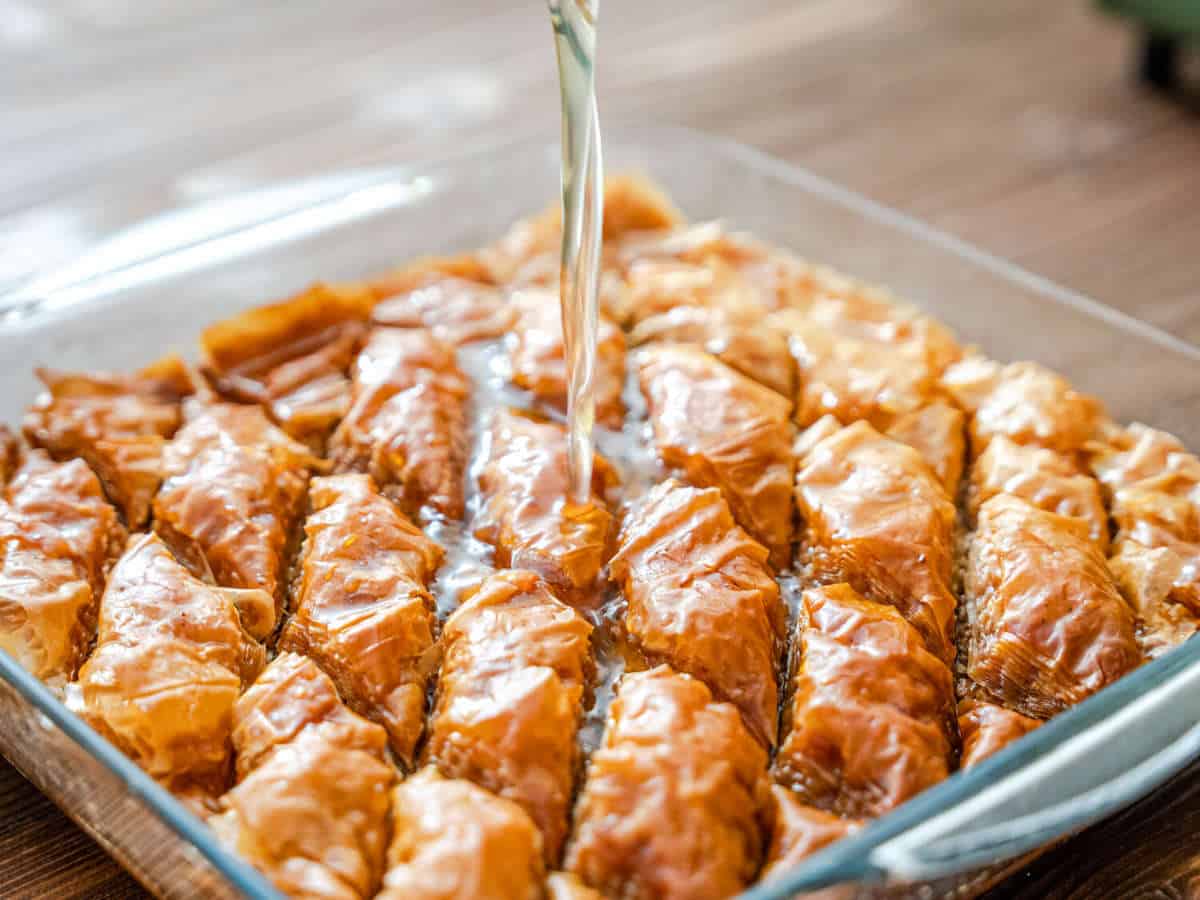 Baked baklava getting drizzled with honey sauce.