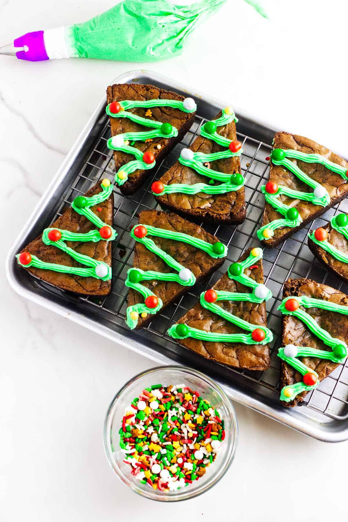 Christmas tree brownies on a cooling rack getting decorations on them.