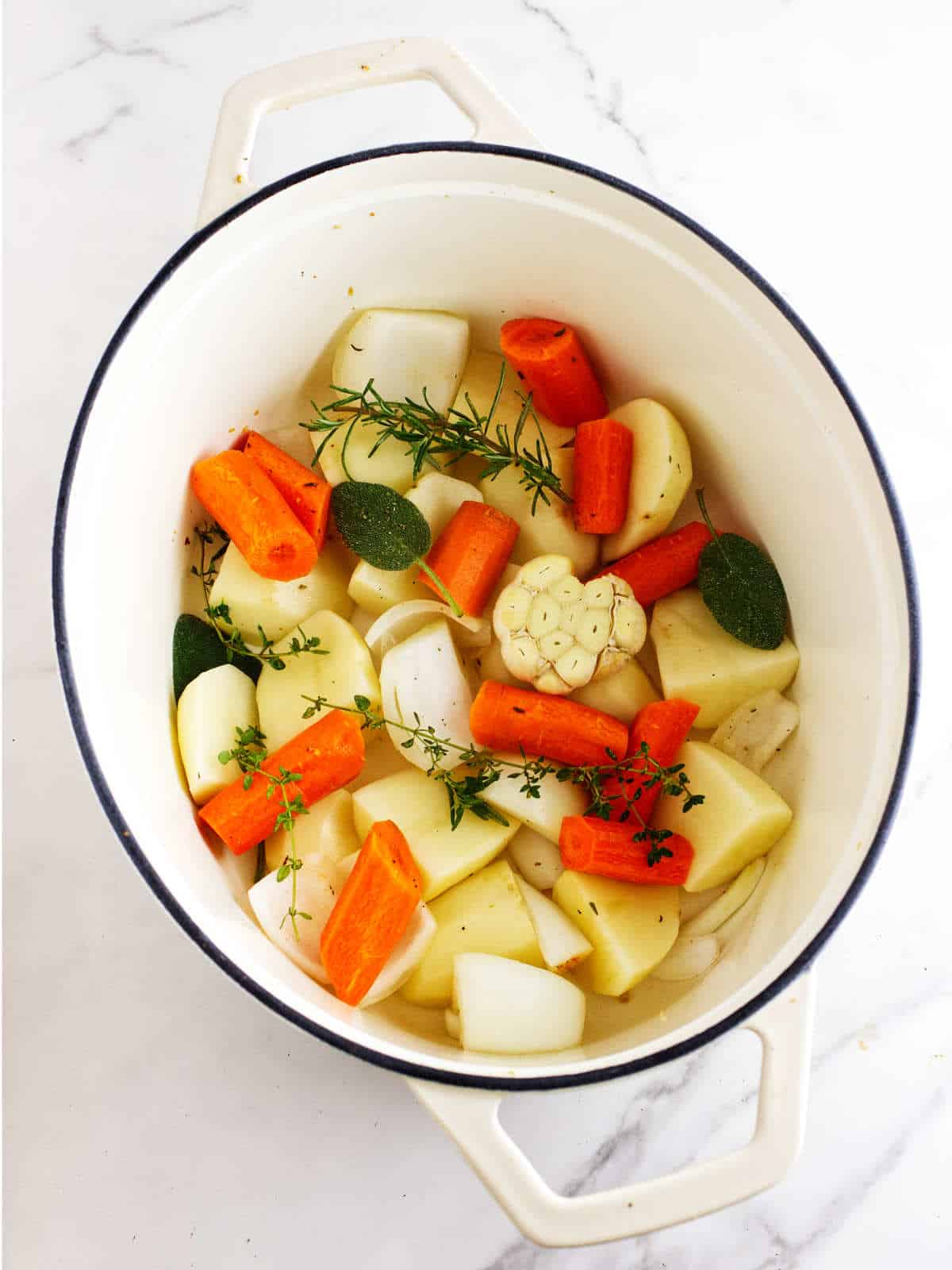 Bottom of a Dutch oven pot with some vegetables and aromatic herbs.