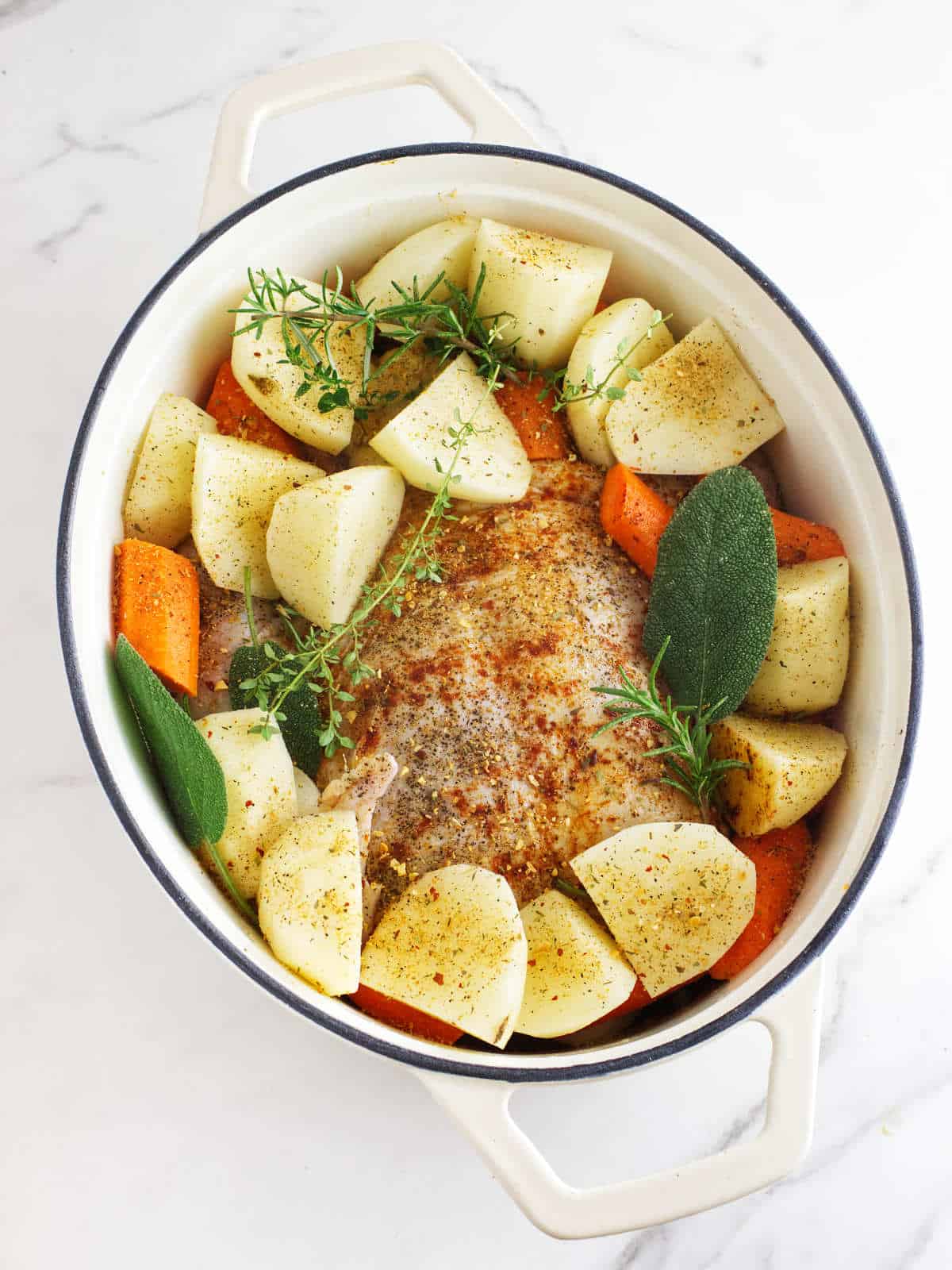 Dutch oven with seasoned raw chicken, quartered potatoes, and carrot chunks.