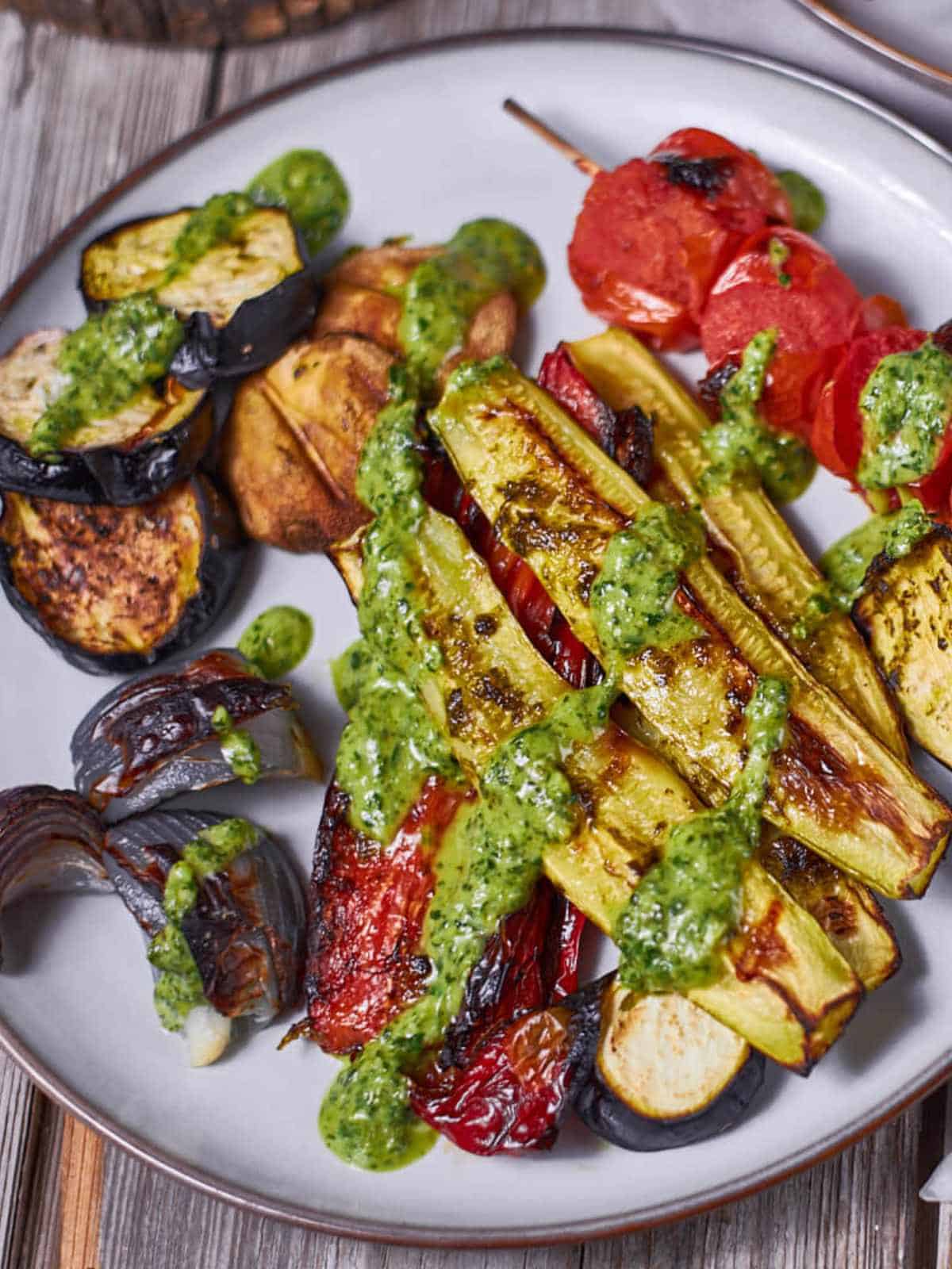 grilled Mediterranean vegetables on a platter with a green sauce on top.