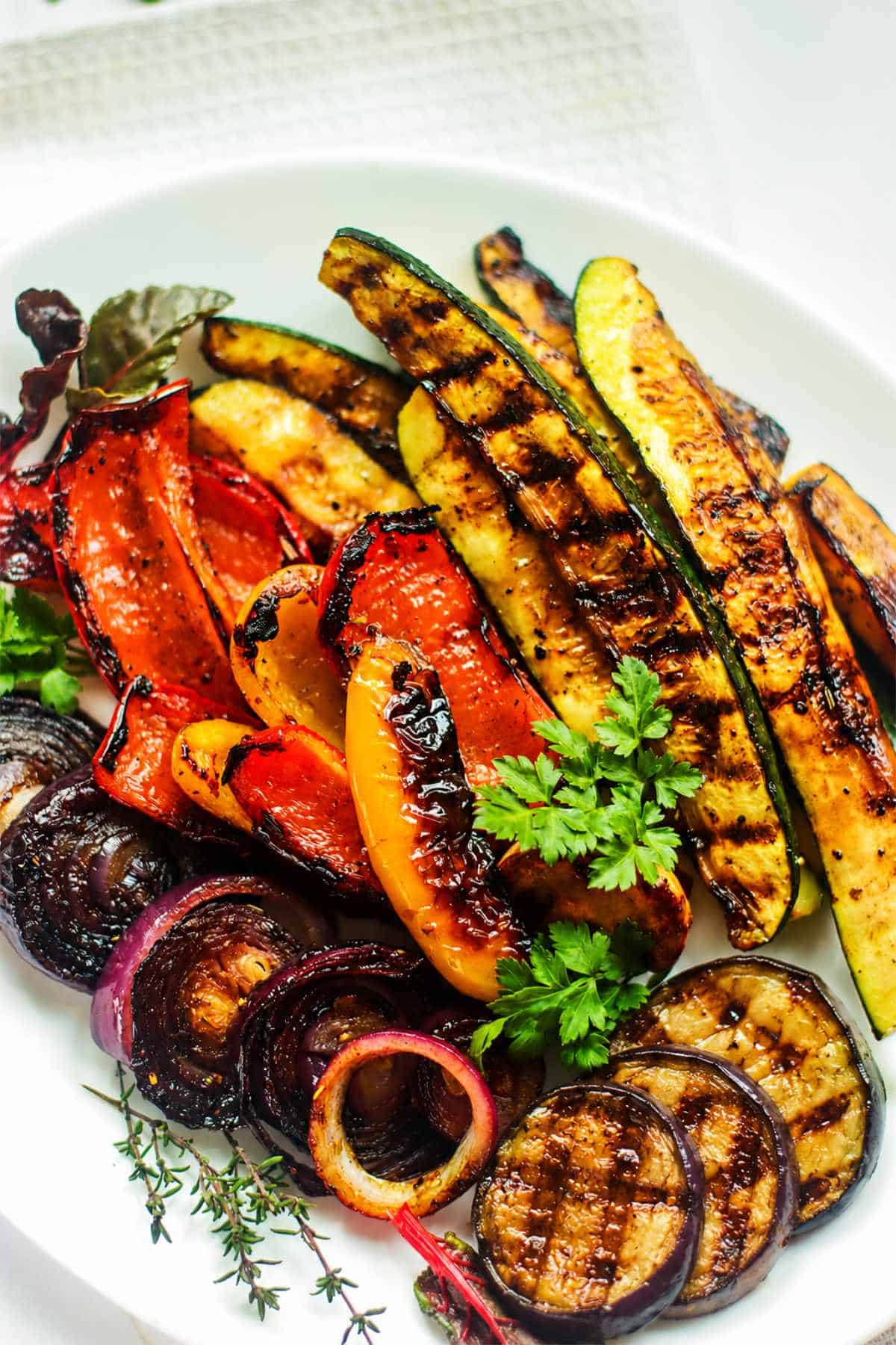 Grilled Mediterranean vegetables with zucchini, peppers, red onion, eggplant, and parsley on a white plate.
