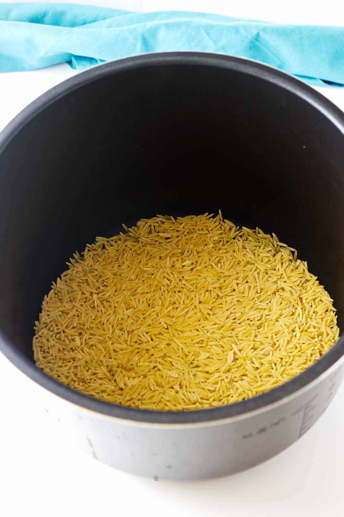 raw orzo measured into an instant pot with some olive oil.