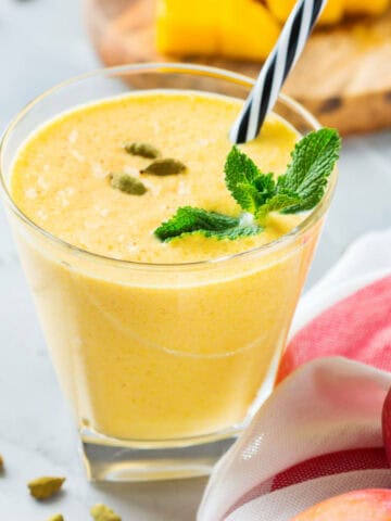 Healthy organic mango lassi, smoothie, shake, indian drink beverage with yogurt and fresh ripe fruits on a kitchen table.