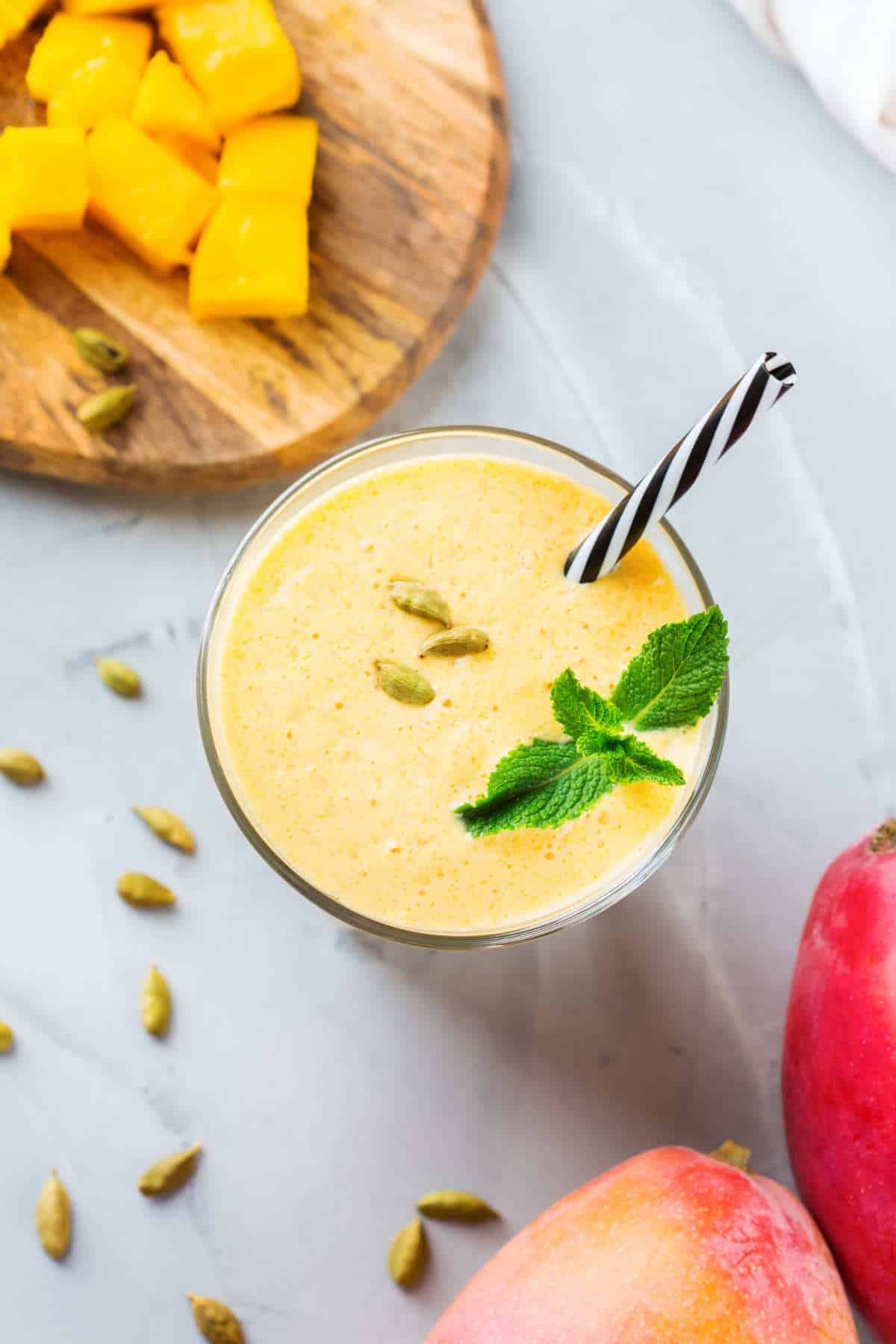 Healthy organic mango lassi, smoothie, shake, indian drink beverage with yogurt and fresh ripe fruits on a kitchen table.