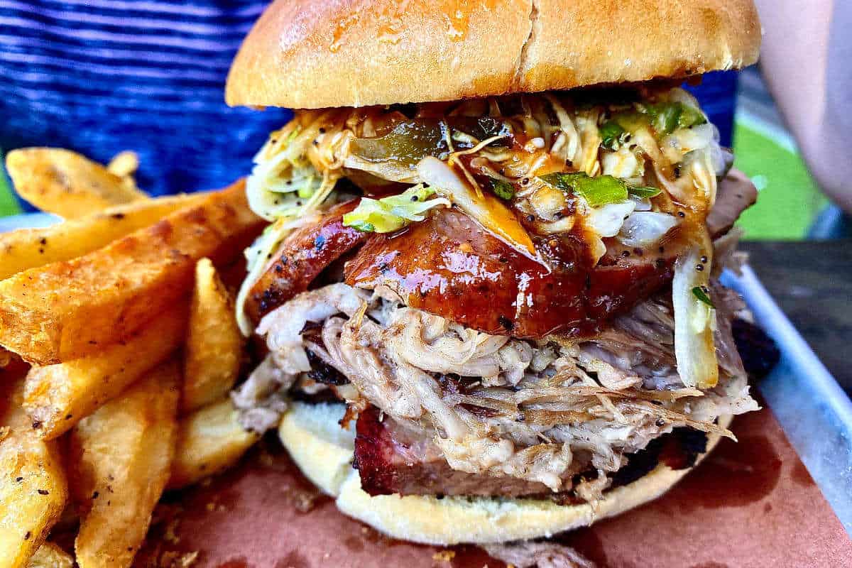 A loaded 3-meat sandwich with slaw on a toasted bun with seasoned French fries.