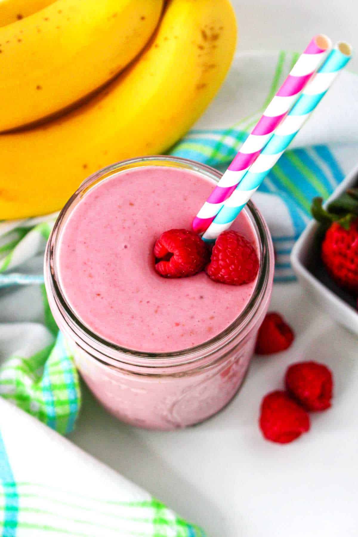 small mason jar filled with a banana raspberry smoothie with a straw in it.