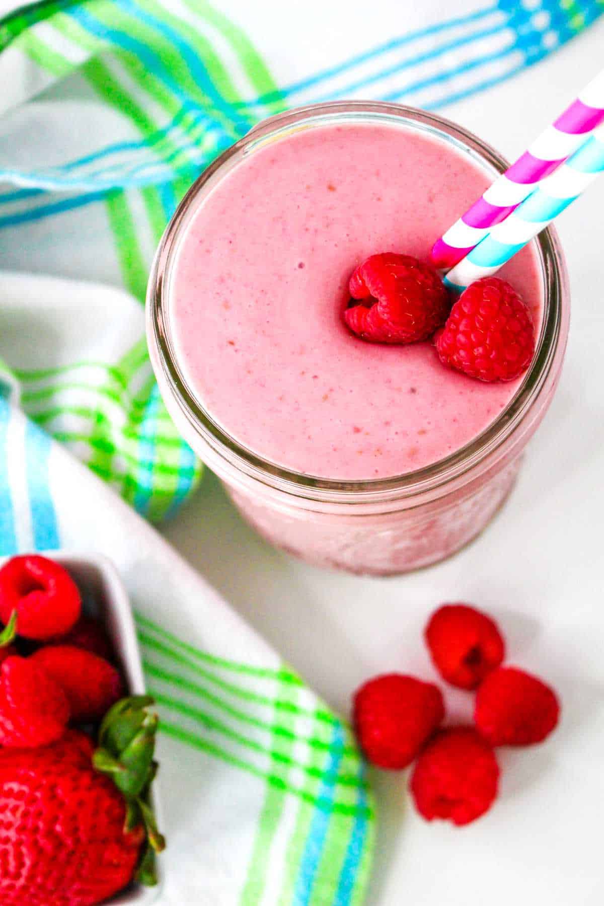 small mason jar filled with a banana raspberry smoothie with a straw in it.