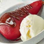 Pear poached in red wine, dessert decorated with ice cream and melted chocolate.