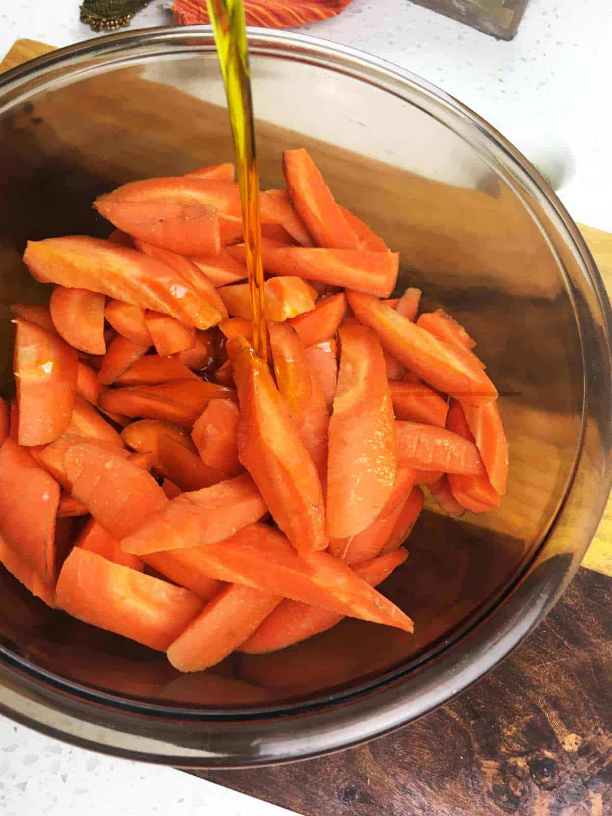 Adding oil to a bowl of cut carrots.