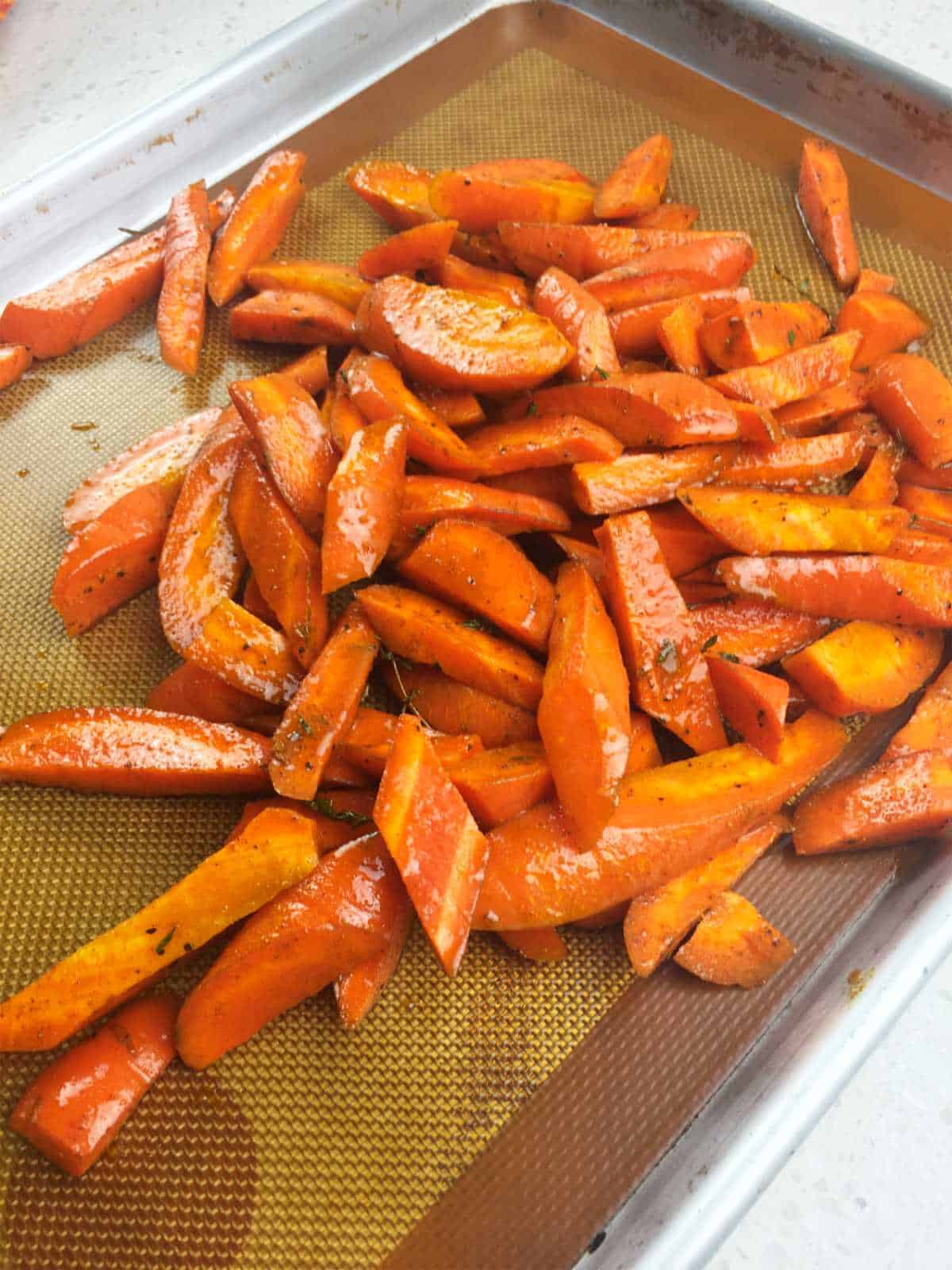 seasoned cut carrots spread out on a sheet pan for roasting.