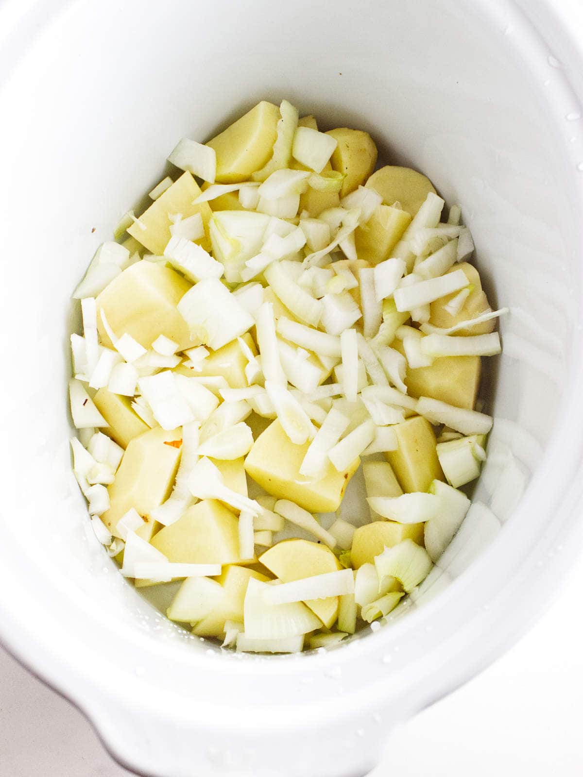 Potatoes and onions layered at the bottom of a slow cooker.