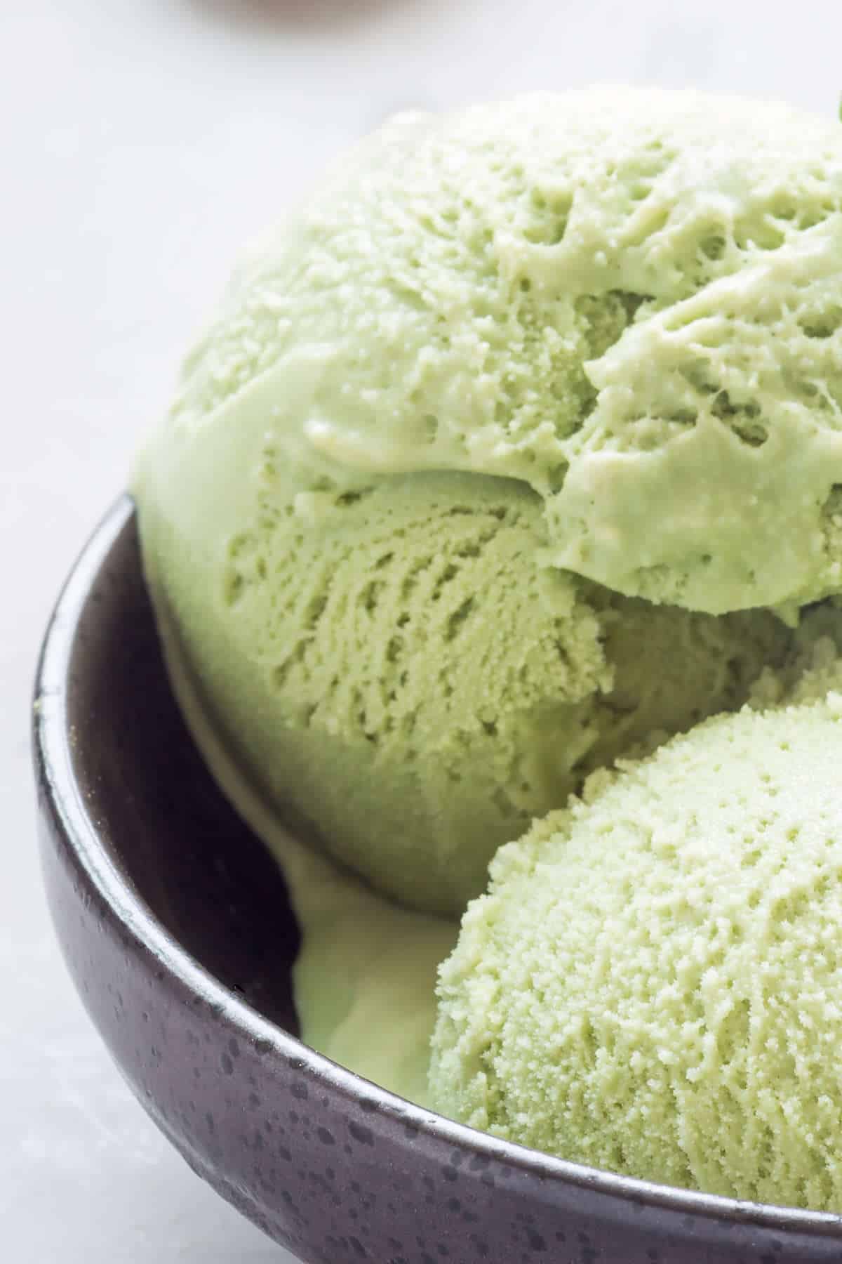 Matcha green tea ice cream balls in black bowl.