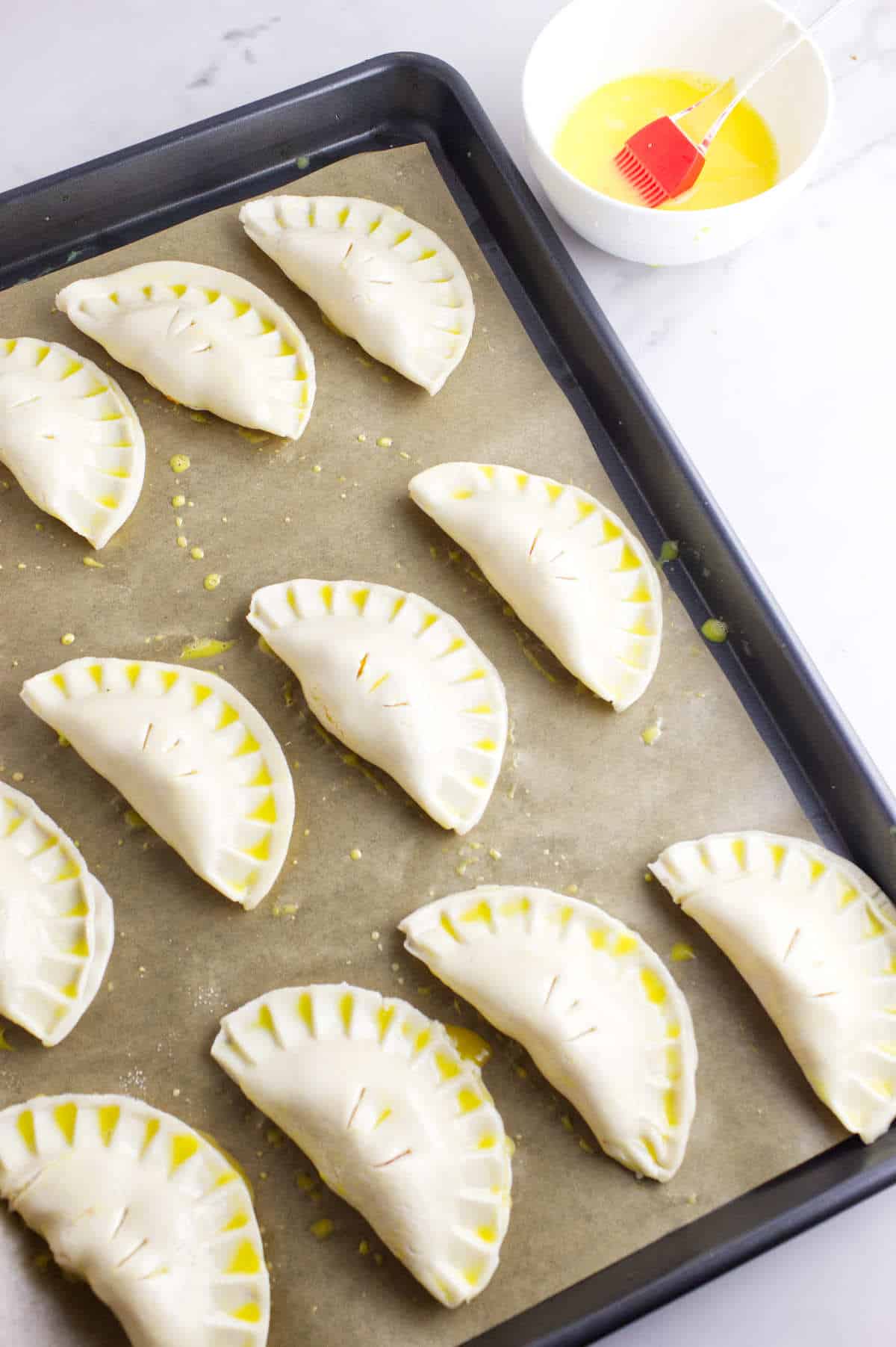 hand pies brushed with an egg wash on a baking sheet.