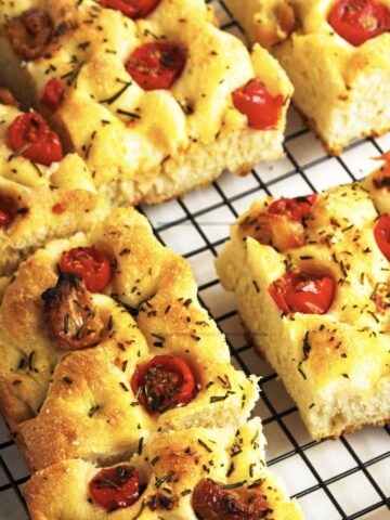 focaccia bread topped with roasted garlic and cherry tomatoes cooling on a rack.