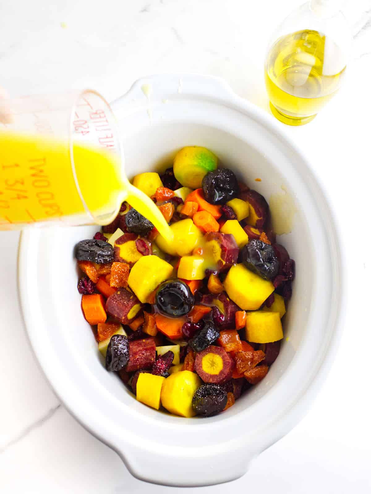 pouring orange juice over cut carrots, sweet potatoes, and spices.