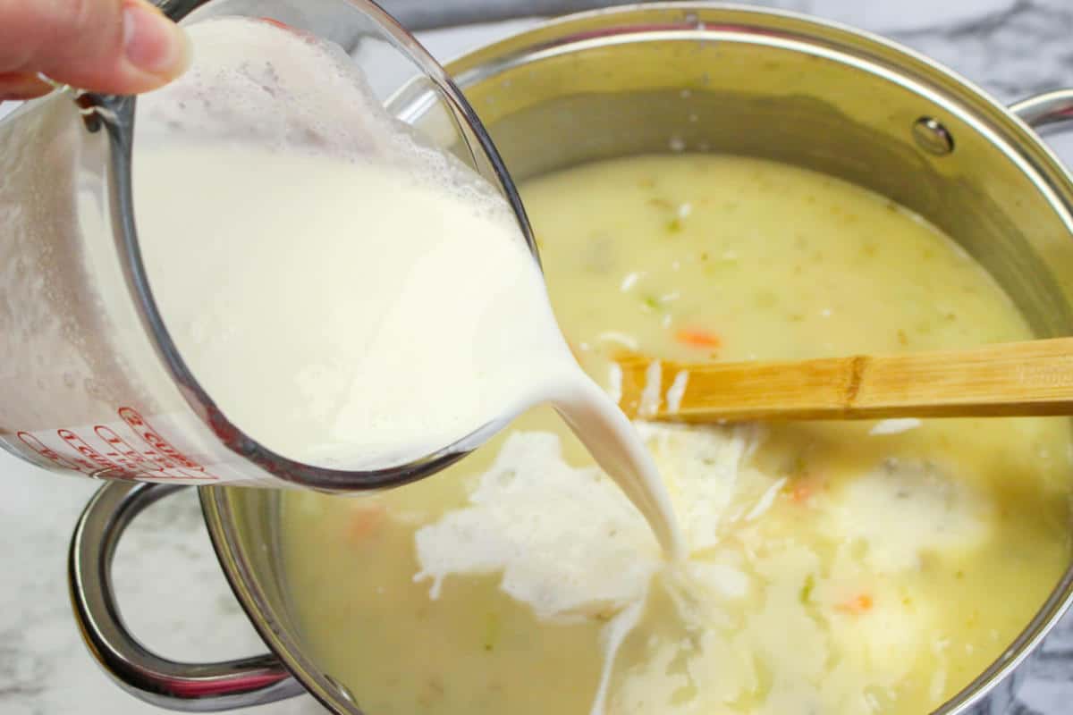 Pouring in cream to pot of wild rice and broth soup.