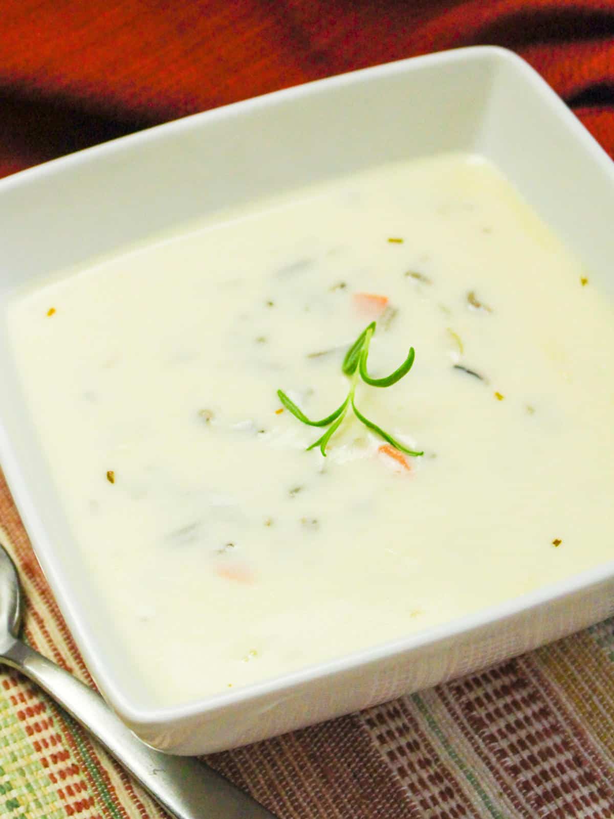 creamy wild rice soup garnished with rosemary.