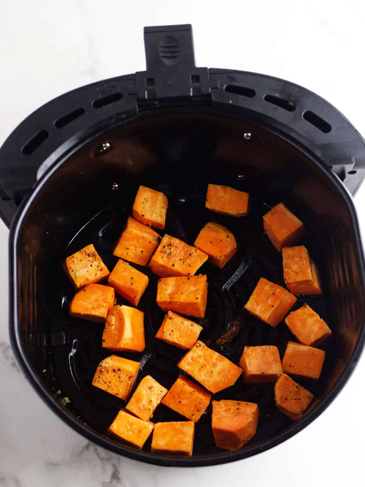 Sweet potato cubes spread out in an air fryer basket.