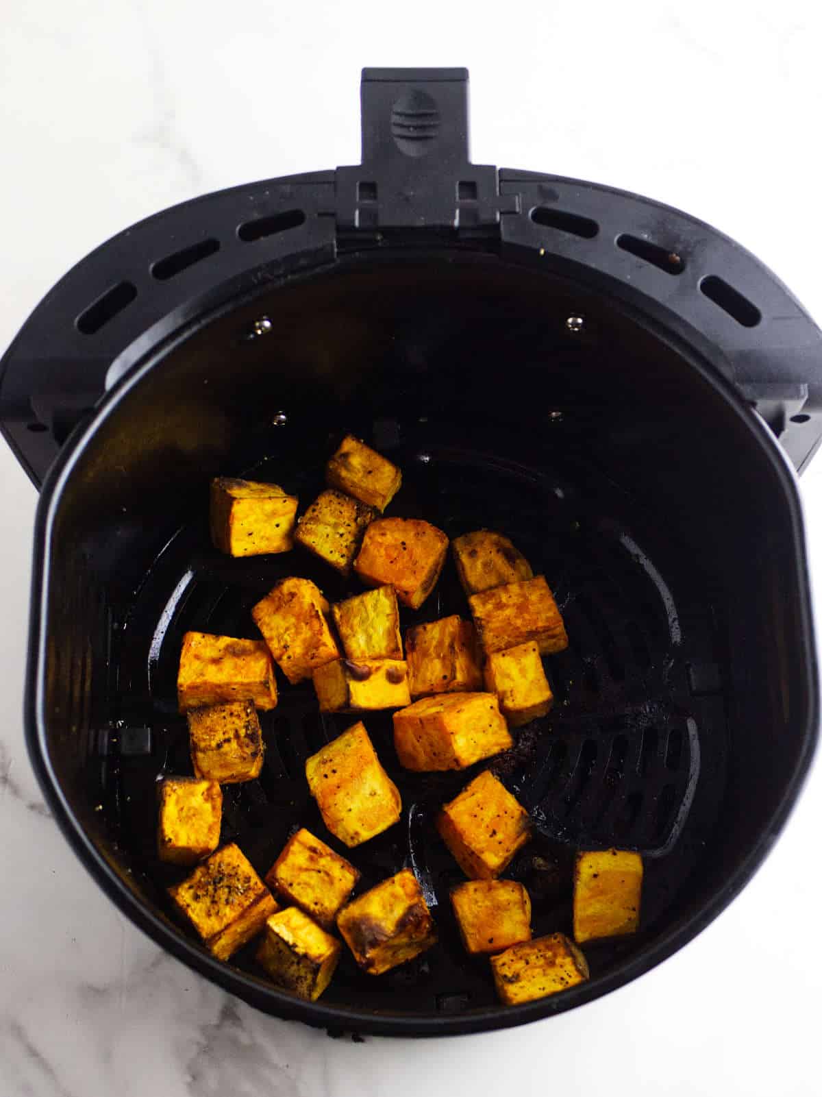 air fried sweet potato cubes in an air fryer basket.