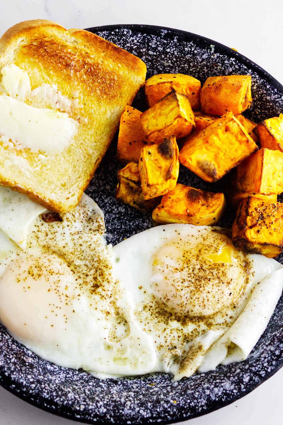 air fryer sweet potato cubes on a plate with fried eggs and buttered toast.