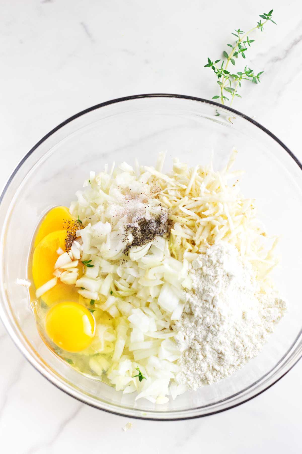 eggs, flour, salt, pepper, and onion with shredded celery root in a bowl.