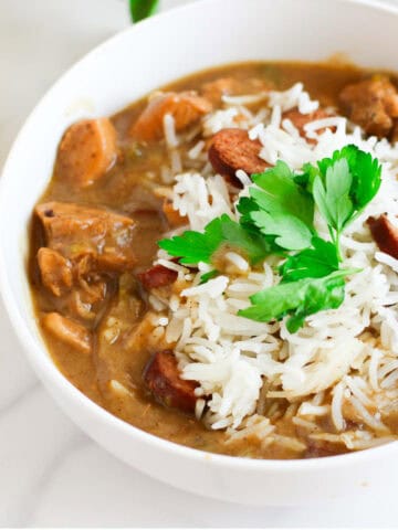 bowl of chicken and sausage gumbo with cornbread nearby.