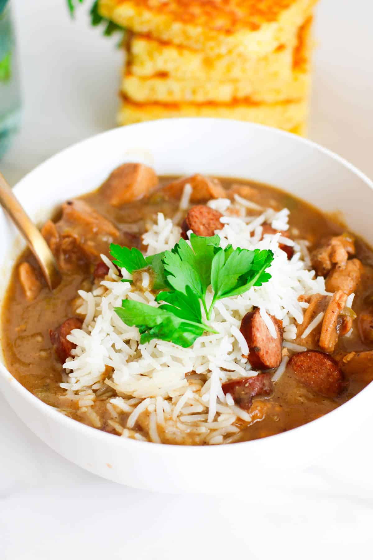 bowl of chicken and sausage gumbo with cornbread nearby.