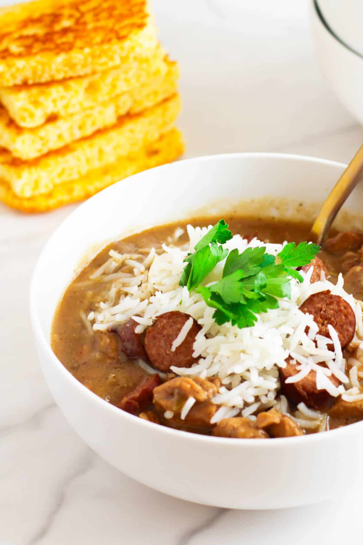 bowl of chicken and sausage gumbo with cornbread nearby.
