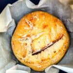 Golden brown baked sourdough boule set inside a parchment paper lined cast iron Dutch oven.