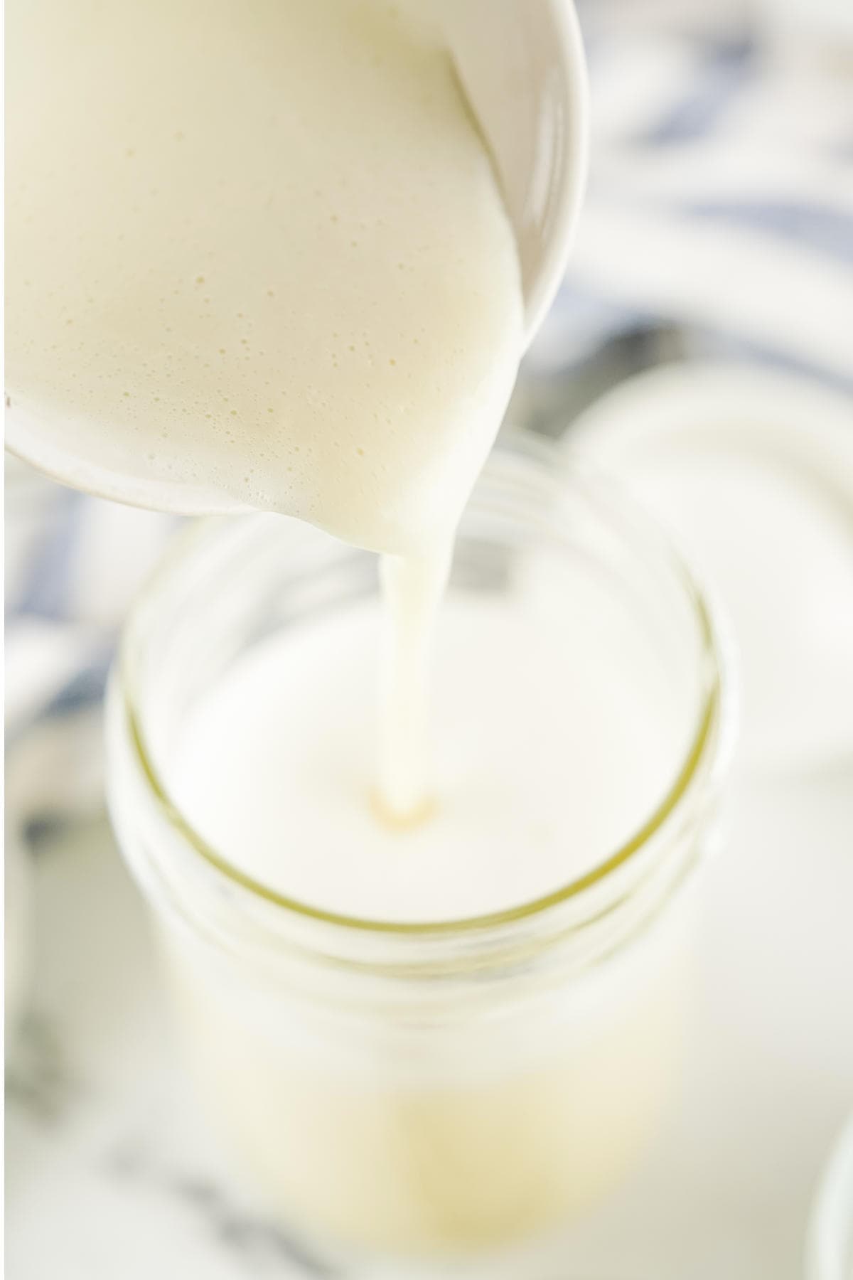 Pouring homemade sweetened condensed milk into a mason jar for storage.