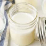 Pouring homemade sweetened condensed milk into a mason jar for storage.