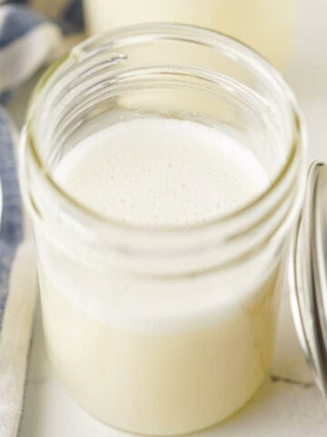 Pouring homemade sweetened condensed milk into a mason jar for storage.