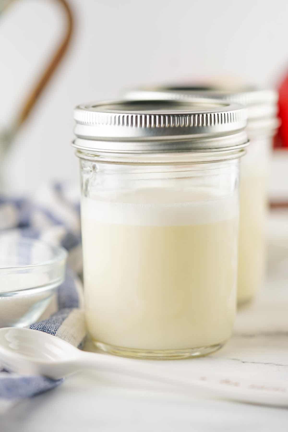 Pouring homemade sweetened condensed milk into a mason jar for storage.