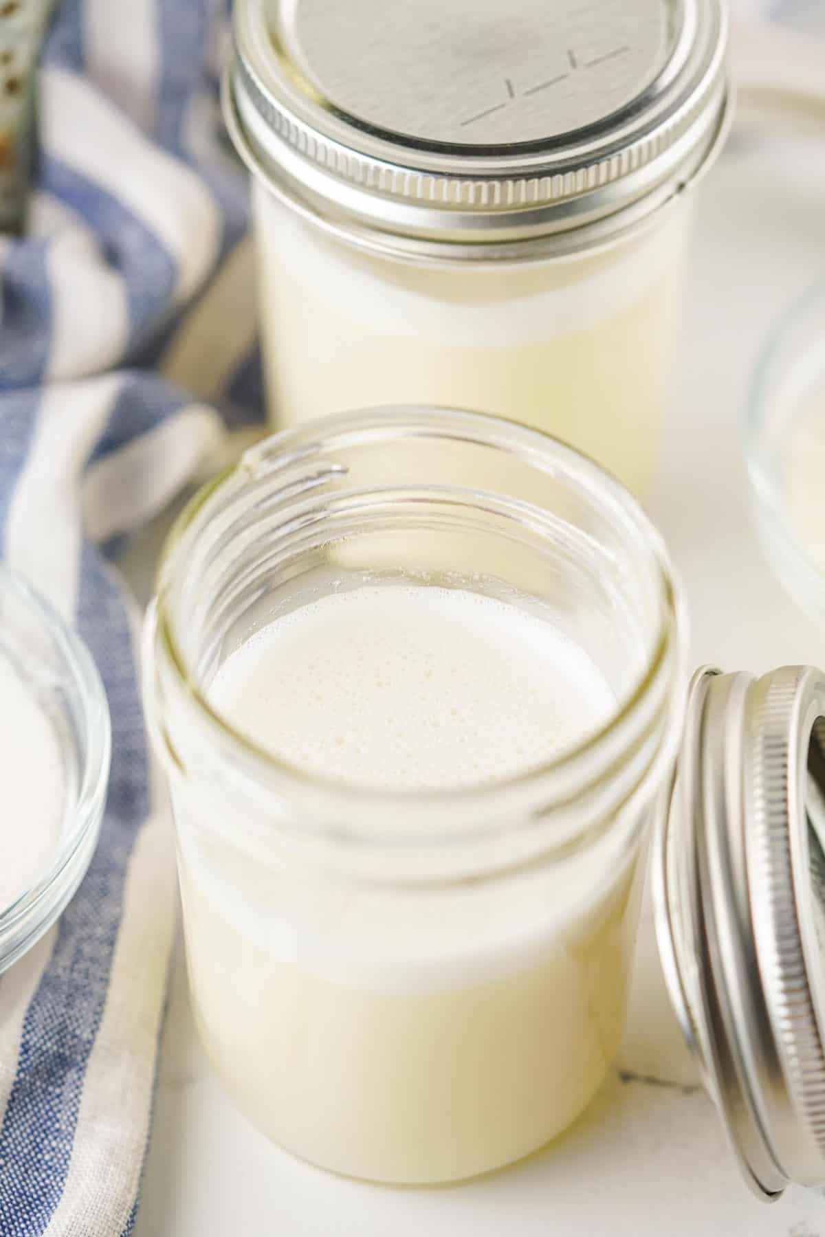 Pouring homemade sweetened condensed milk into a mason jar for storage.