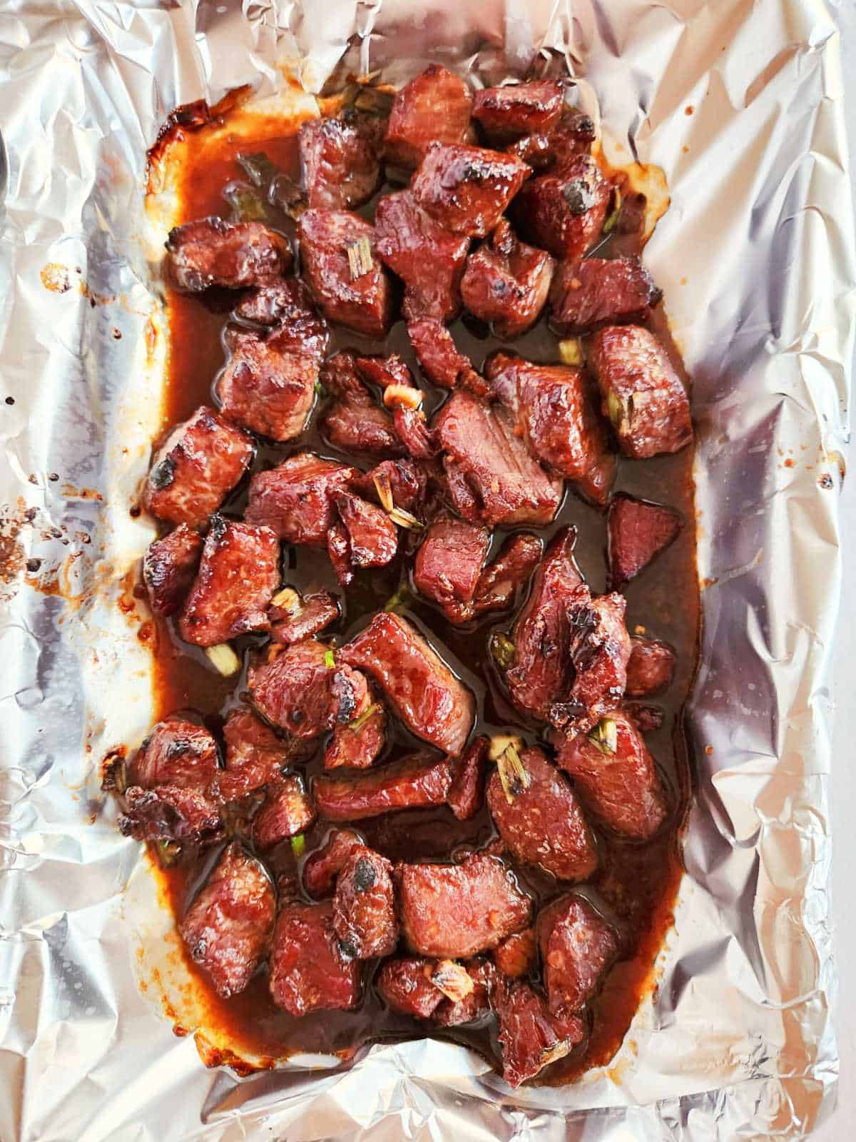 cooked beef bulgogi on a foil lined pan on the grill.