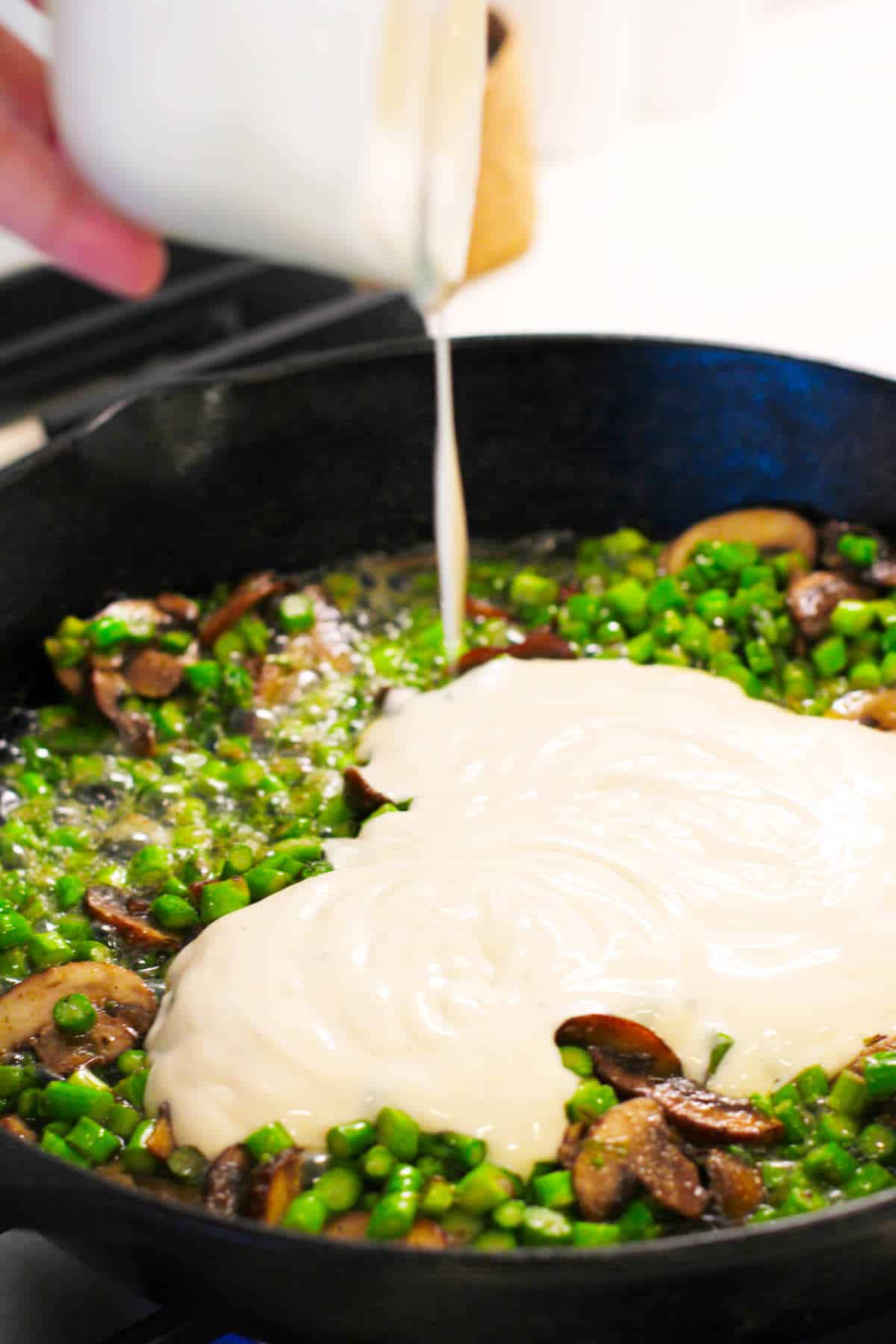 Adding a jar of Alfredo sauce to skillet with mushrooms and asparagus.