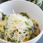 Parmesan topped mushrooms and asparagus topped pasta in a bowl.