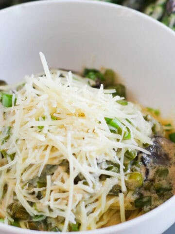 Parmesan topped mushrooms and asparagus topped pasta in a bowl.