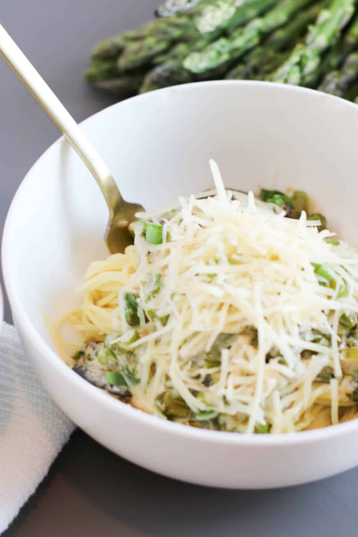 Parmesan topped mushrooms and asparagus topped pasta in a bowl.
