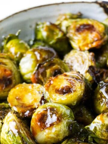 Serving bowl of roasted Brussel sprout drizzled with balsamic vinegar.