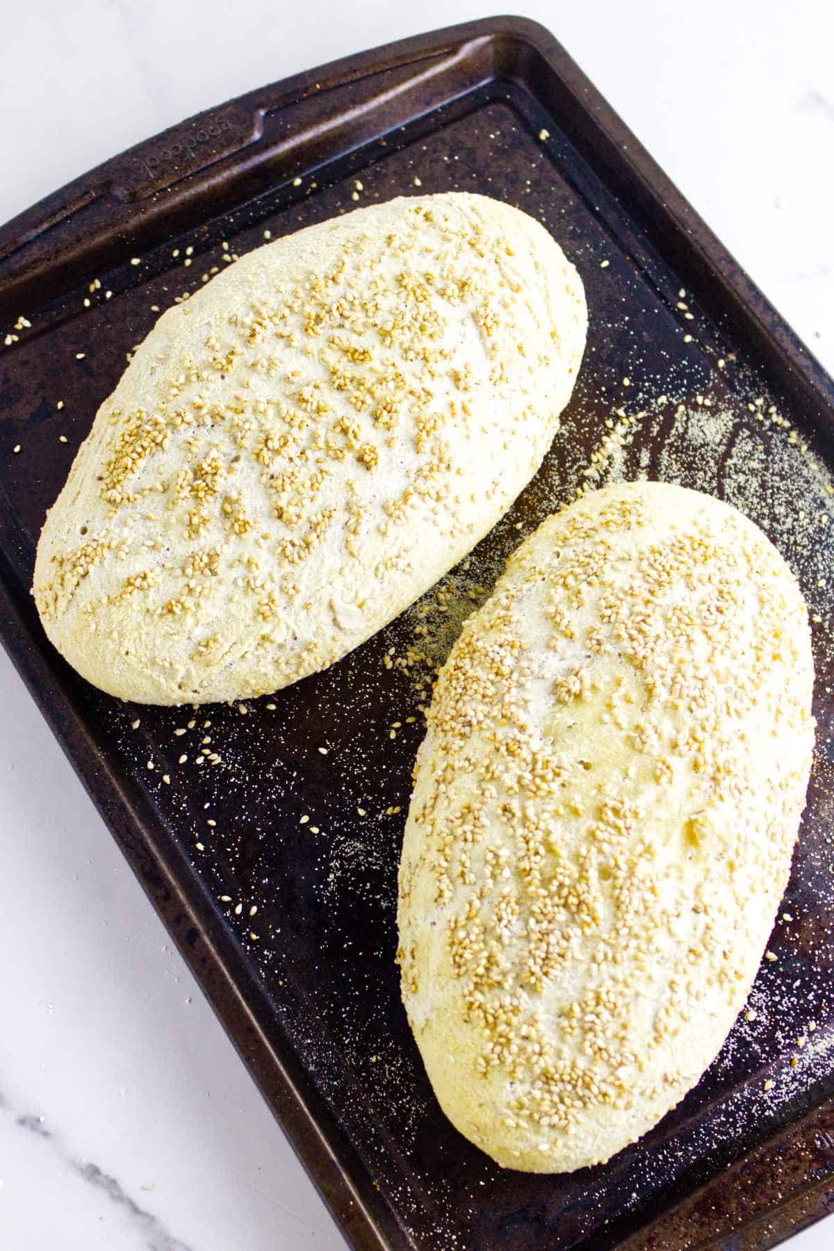 two risen loaves of semolina dough on a baking sheet.