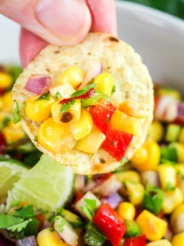 round tortilla chip dipping into chili corn salsa.