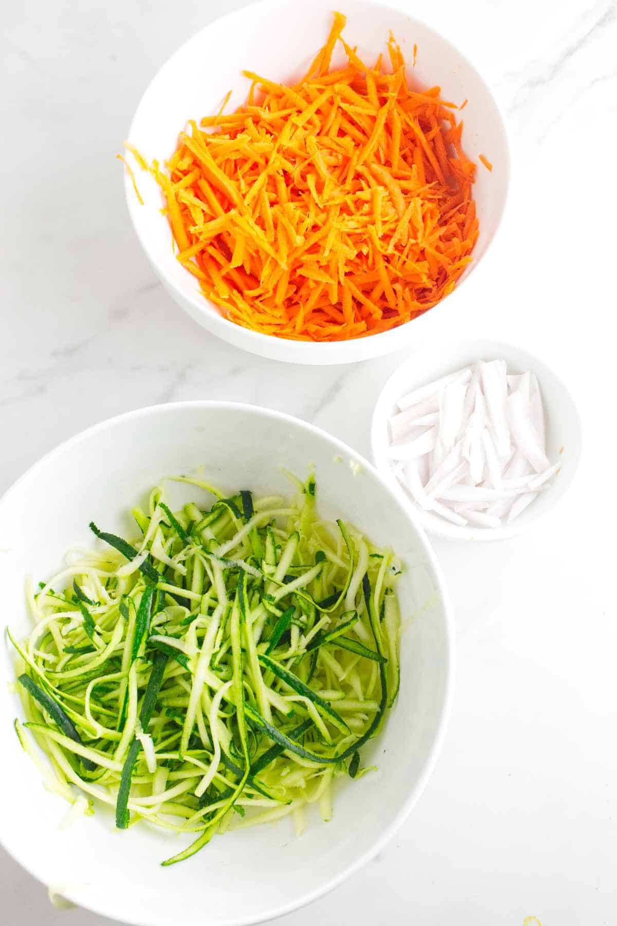 bowls of shredded carrot, zucchini, and shallot.