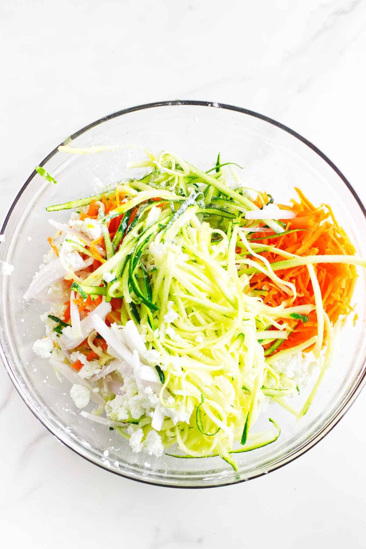 Bowl of shredded zucchini, carrot, shallots, and crumbled feta cheese.