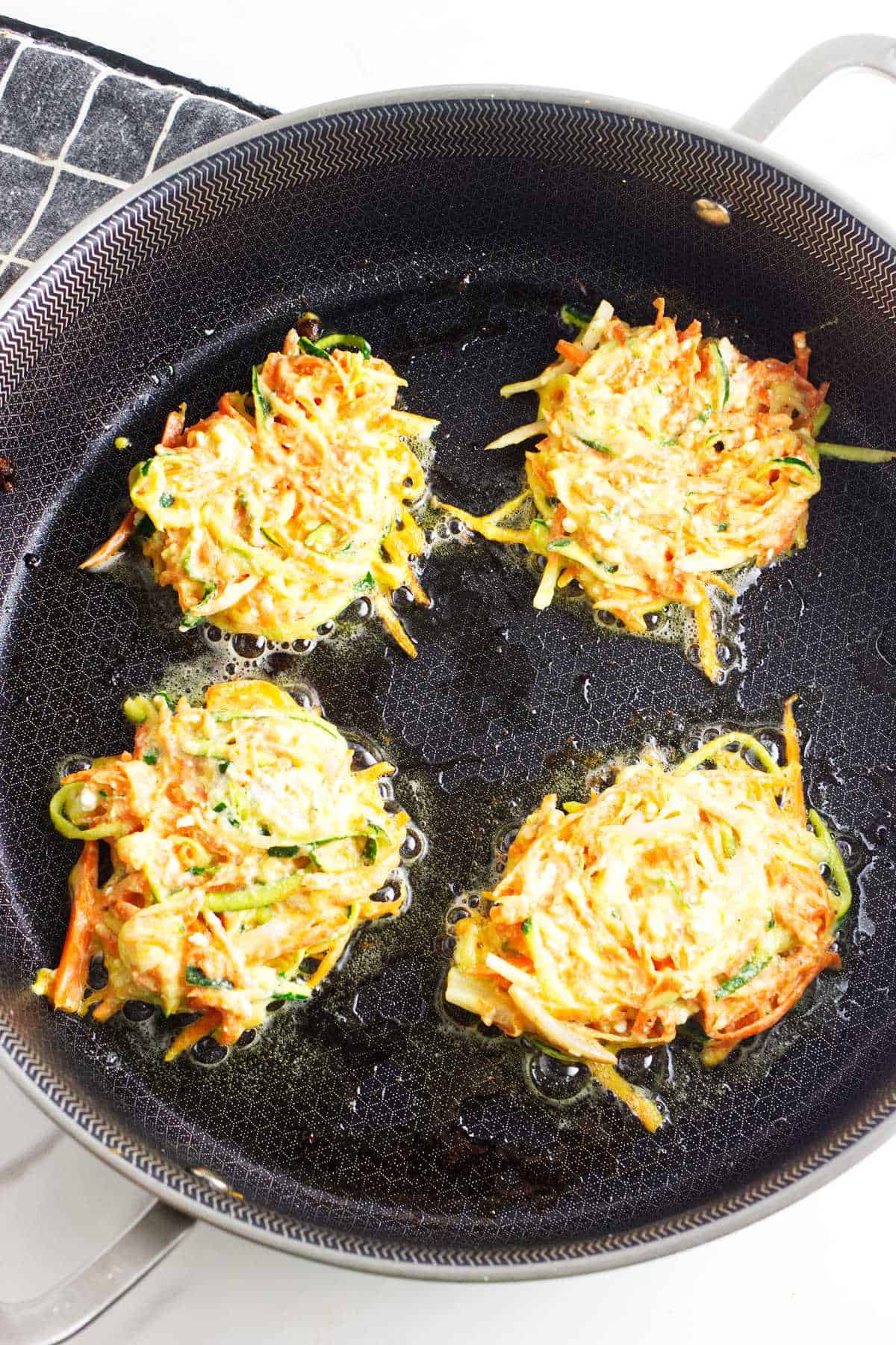 frying zucchini carrot latkes in a cast iron skillet.