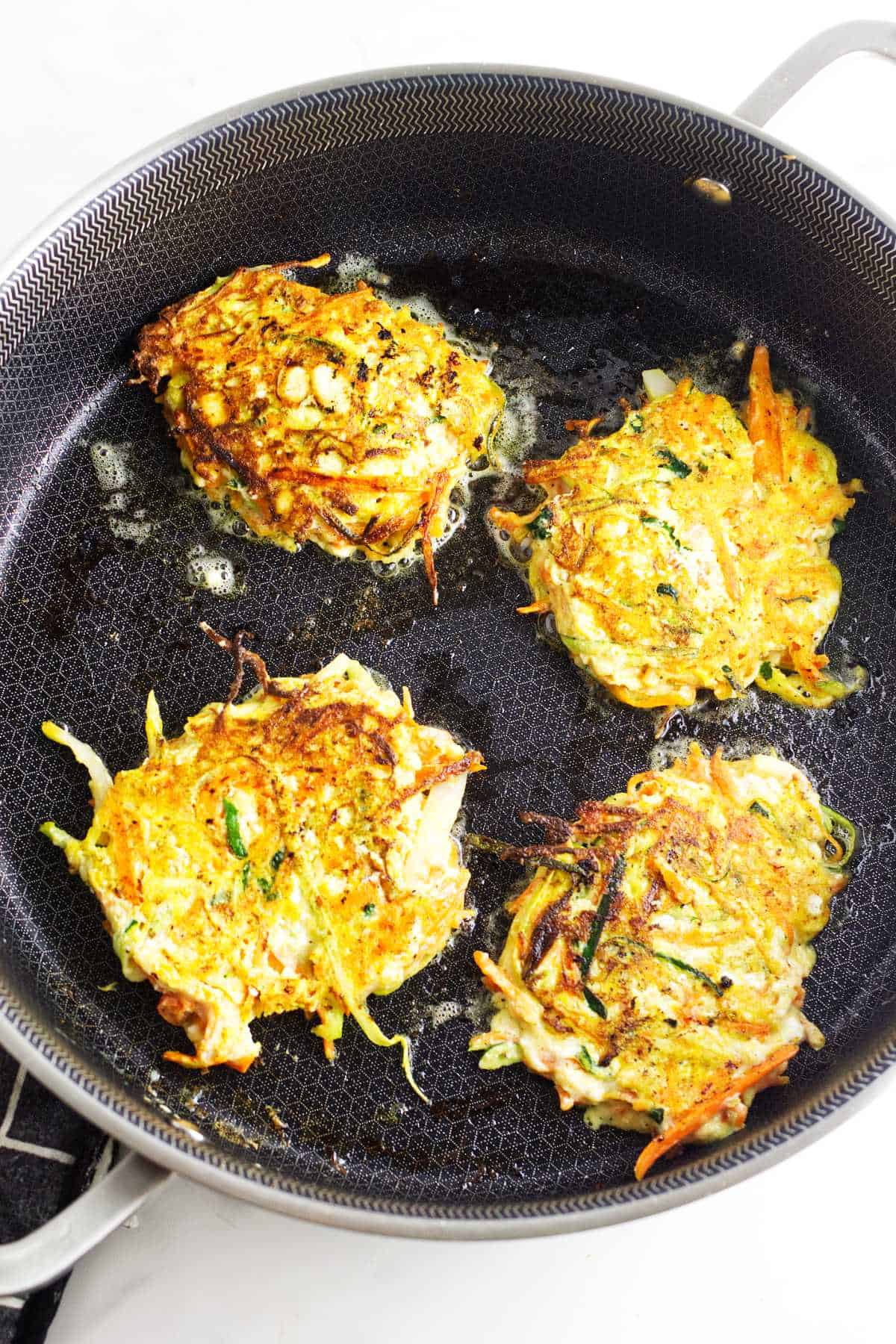 frying zucchini carrot latkes in a cast iron skillet.