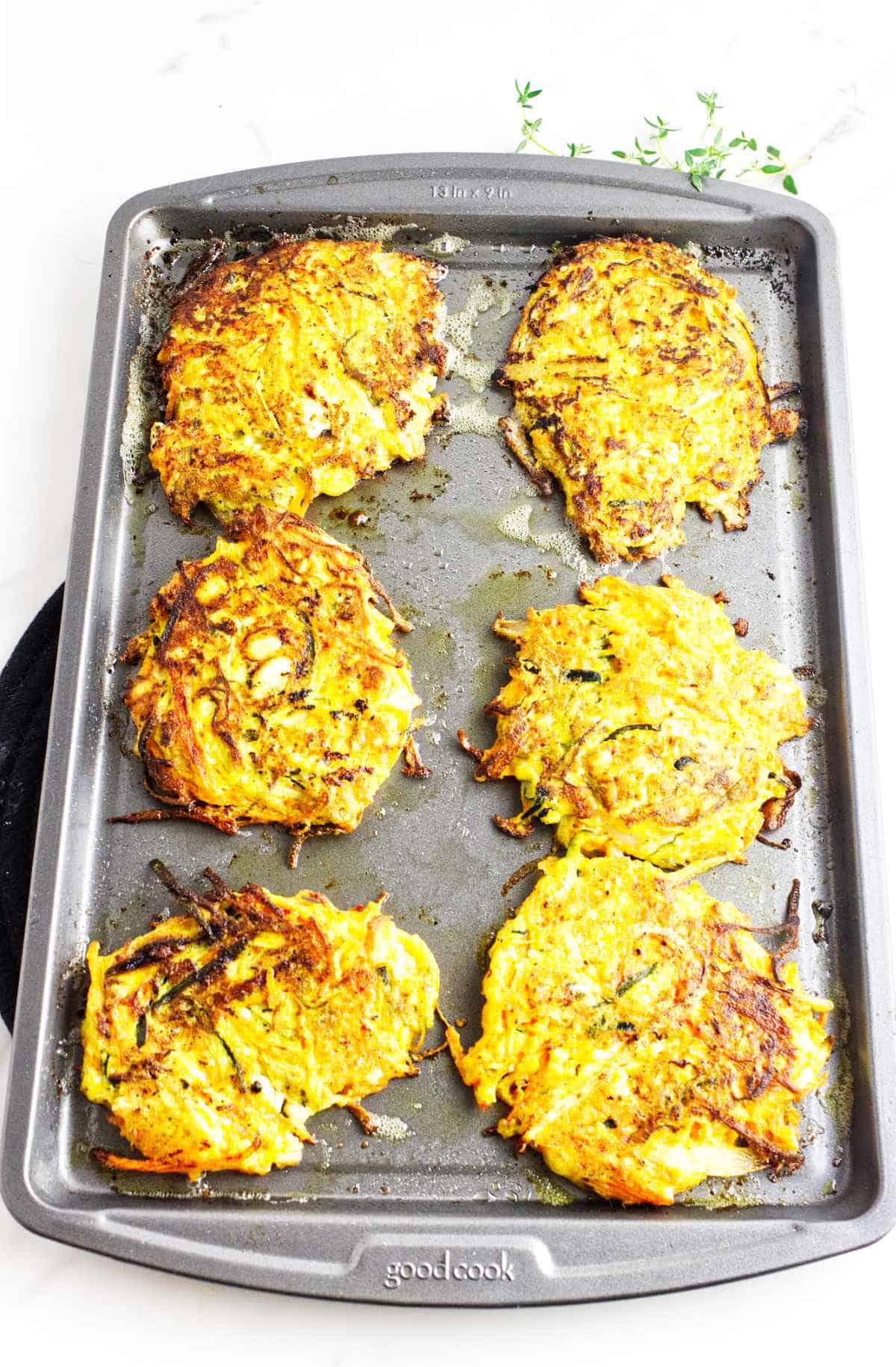 Placing partially cooked latkes on a baking sheet to finish cooking in the oven.