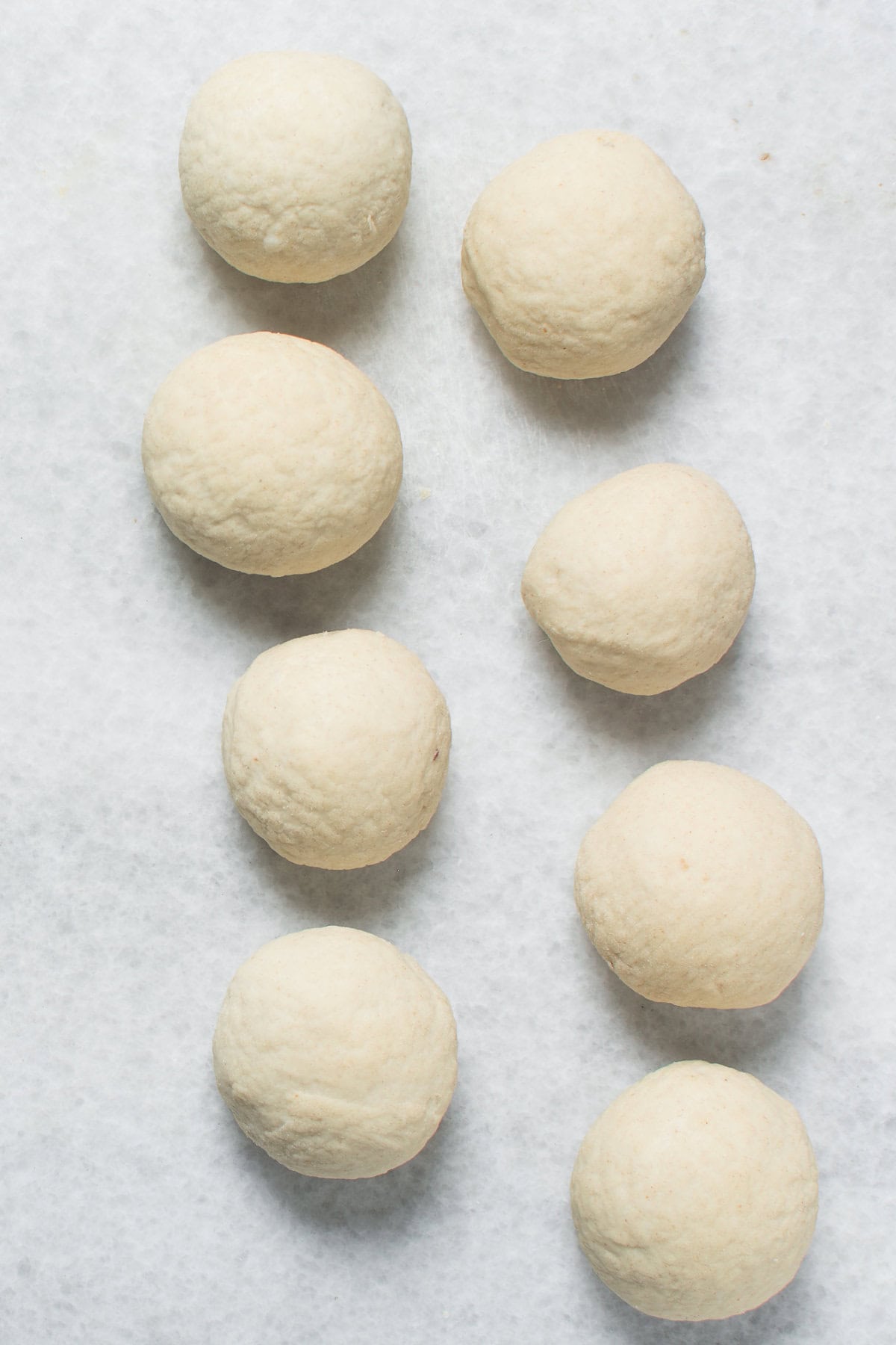 Eight evenly spaced dough balls, resembling Chinese steamed buns, are arranged in two vertical columns on a white, lightly textured surface.